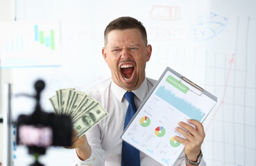 Angry businness vlogger hold in hands dollars and financial statistics chart portrait. Financial...