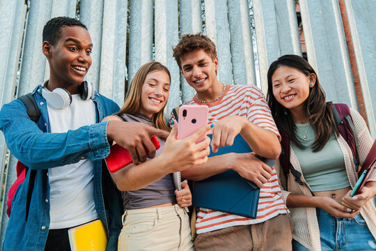 Group of young diverse high school students smiling and having fun watching a social media app on a smartphone. University classmates using a cellphone. Happy friends browsing on internet with a phone