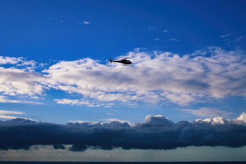 Silhouette of a helicopter flying over the sea with dramatic clouds