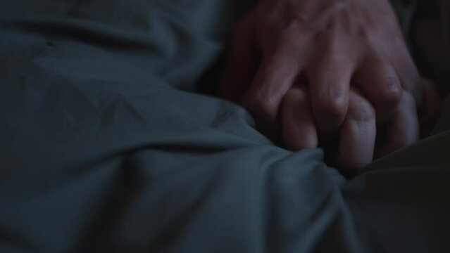 Dark slow mo shot of a sign of love. Two hands come together on the bed sheets and they huddle together. Intercourse between a man and a woman. Close shot of hands
