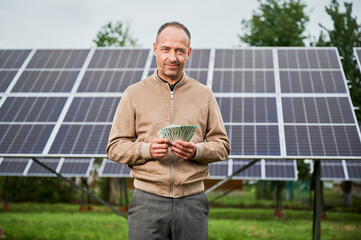 Young man happy about his profit from solar panels. Man smiling with his earnings in hands....