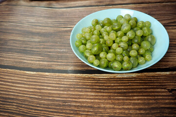 There are a lot of green gooseberries on a brown wooden table in a blue plate. sour sweet berry. vitamins. poster , copy space