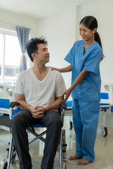 Obraz premium A young female doctor is caring for a man in a wheelchair in the house. Positive and happy Asian female nurse or physical therapist in blue uniform caring for male patient in close proximity.