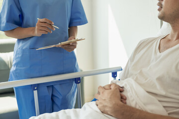 Asian female nurse and young male patient lying in bed while checking his pulse Consult and explain, take notes and help in the medical health concept ward. © MrAshi