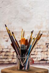 various brushes in a glass jar on the background of a brick wall, painting supplies