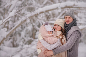 Obraz premium A beautiful happy family stands in the winter forest and holds their daughter in their arms. Winter's Tale. Snowy forest. A lot of snow.Trees in the snow. Dad hugs his daughter tenderly.winter clothes
