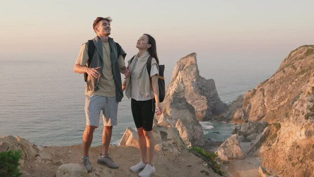 Immerse in nature's embrace. A couple stands on the coast, breathing in fresh air, wearing hiking clothes, and savoring the beauty of the sunset