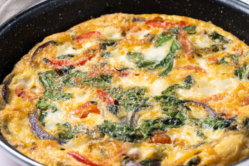 Italian Frittata made with spinach, tomatoes, onion and peppers isolated on white background. Close up
