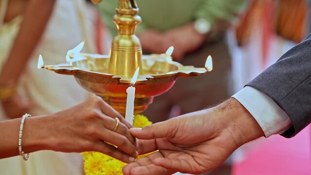 Closeup of male and female hands lighting diya oil lamp with a lit candle at event