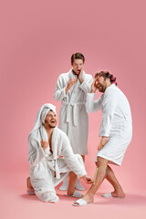 Friends in bathrobes meeting at home spa, doing depilation, drinking champagne against pink background. Concept of leisure activity, fun, bachelor party, friendship, spa, cosmetology