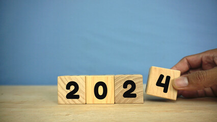 hand puts the number 4 for the year 2024 on a wooden cube