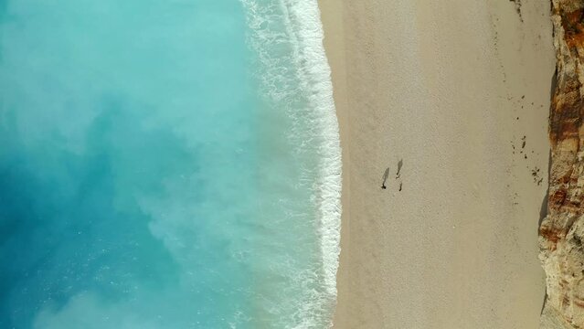 Drone aerial top view of couple walking on iconic Porto Katsiki beach in Lefkada island with turquoise water, in Greece