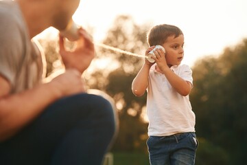 With string can phone. Father and little son are playing and having fun outdoors - obrazy, fototapety, plakaty