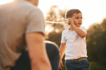 Fun, holding and using string can phone. Father and little son are playing outdoors
