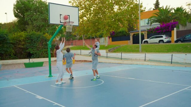 Sport And Family Friendship. Multigenerational Family Playing Basketball On Outdoor Court. The Family Spends Their Free Time Together Playing Sports And Playing Basketball On The Basketball Court