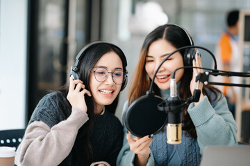 Young woman and Asian woman wearing headphones and doing a live podcast for their channel,...