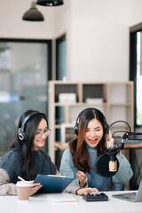 Young woman and Asian woman wearing headphones and doing a live podcast for their channel,...