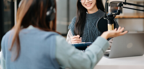 Young woman and Asian woman wearing headphones and doing a live podcast for their channel, communication for radio podcast and technology concept.
