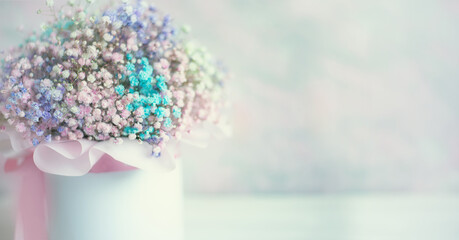 A bouquet of small multi-colored flowers in a cardboard box on a delicate pink background. Bouquet...