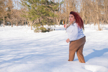 A fat red-haired woman in a white sweatshirt walks through snowdrifts. 