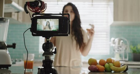 Woman, camera and live streaming in kitchen, food blog and tutorial or teaching at home. Female influencer, webinar and vlogger or technology for video recording, juice and fruit for nutrition