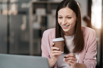 portrait of a business woman Self-confident young woman sit holding coffee mug and working laptop. ...