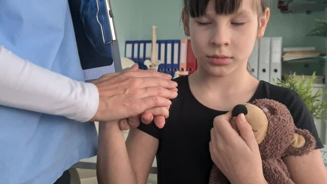Hands of female doctor hold hand of child patient with toy. Pediatrician and medical care for children