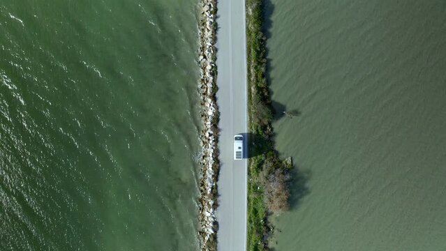 Drone aerial top view of camper van with solar panels driving in Koronisia road in the middle of the sea, in Greece