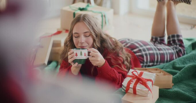 Beautiful woman drinking coffee while lying on floor during Christmas