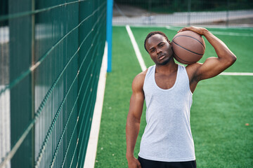 Front view. Young black man is with basketball ball outdoors - Powered by Adobe