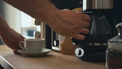 Side stab footage of male hand taking coffeemaker kettle and pouring brewed coffee into white porcelain cup in modern kitchen