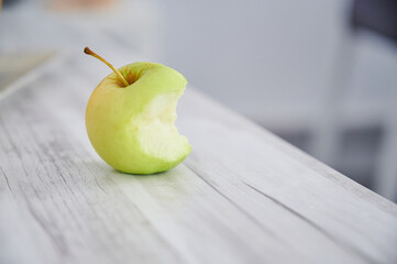 Isolated small bitten fresh apple on a grey wooden table. Vegan habits and 