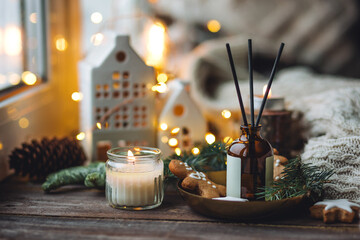 Home aroma diffuser with sticks for cozy holiday Christmas atmosphere. Pine fir tree fresh scent, sweet smell of homemade gingerbread cookies with cinnamon, anise. Candles, fairy lights as decor