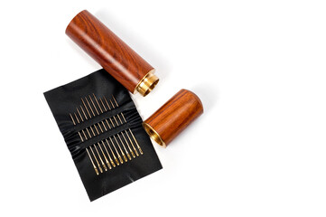 Metal sewing needles for hand sewing on a faux leather base and a container for storing them.