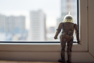 An iron robot stands on the windowsill and looks out the window at the street. The invasion of artificial intelligence. The robot's escape to freedom.
