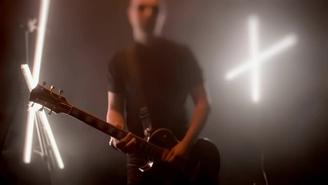 Guitarist plays electronic bass guitar in slow motion. Rock sound concept. Musical solo performance in dark studio with fog smoke and artistic light. Tilt-shift effect