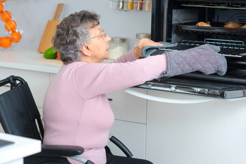 elderly disabled woman in wheelchair using the oven - obrazy, fototapety, plakaty