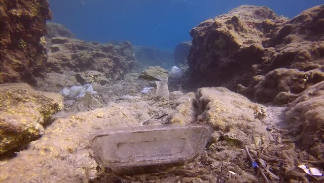 Camera moving forwards low along seabed covered with lots of plastic debris in crevice between rocks. Seafloor covered with wery many plastic garbage polluting Mediterranean Sea