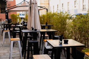 Empty chairs in outdoor cafe or restaurant on summer day. Restaurant black tables waiting for customers, old town