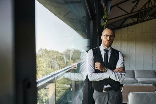 good looking businessman in black smart vest and tie looking at camera standing next to window