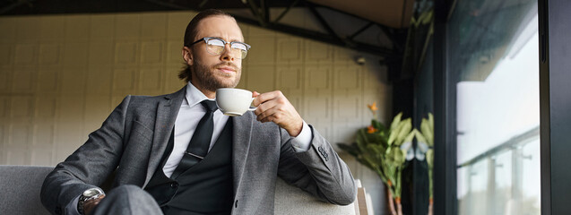 handsome appealing man in gray smart suit drinking tea and looking away, business concept, banner