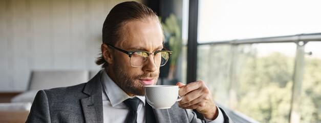 appealing refined businessman with red hair and glasses in smart suit drinking tea, banner