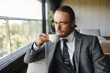 handsome man with dapper style suit with glasses and tie drinking tea on sofa, business concept