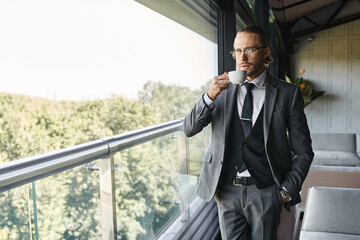 handsome refined man in gray suit with glasses drinking tea with hand in pocket, business concept