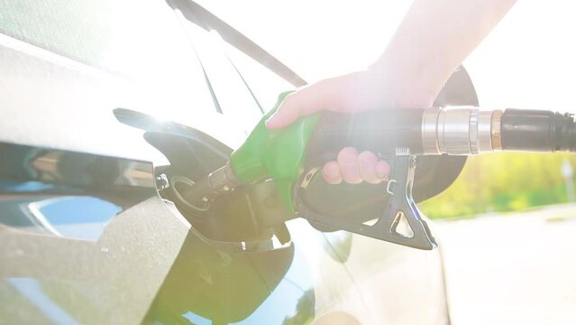 Fuel nozzle in the tank of a car at a gas station. Concept of the cost of gasoline per liter. Gasoline quality, car fuel consumption. A handgun against the backdrop of the sun. Slow motion