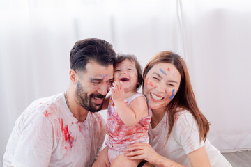 Naughty multicultural family with little toddler having fun laughing playing together at home, Hispanic father and Asian mother spend time with daughter painting faces in weekend holiday love bonding