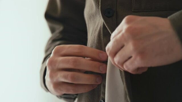 Side tilt closeup of hands buttoning brown shirt while dressing up indoors