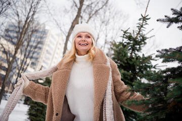 Photo of good mood excited woman wear beige coat having fun hiding between christmas trees outside urban city park