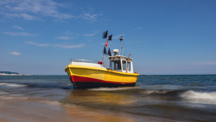 Naklejka na ściany i meble Fishing boat on the beach in Sopot, Poland. Magnificent long exposure calm Baltic Sea. Wallpaper defocused waves. Fishermans sea bay Vacation and holidays. travel attraction tourist destination 