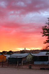 Sunset with a silouette of a cross on top of a church and poor metal shacks in front in Namibia